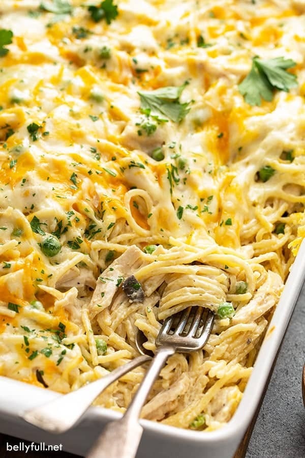 Chicken tetrazzini with cream sauce and chicken on a white casserole dish with spoon and fork.