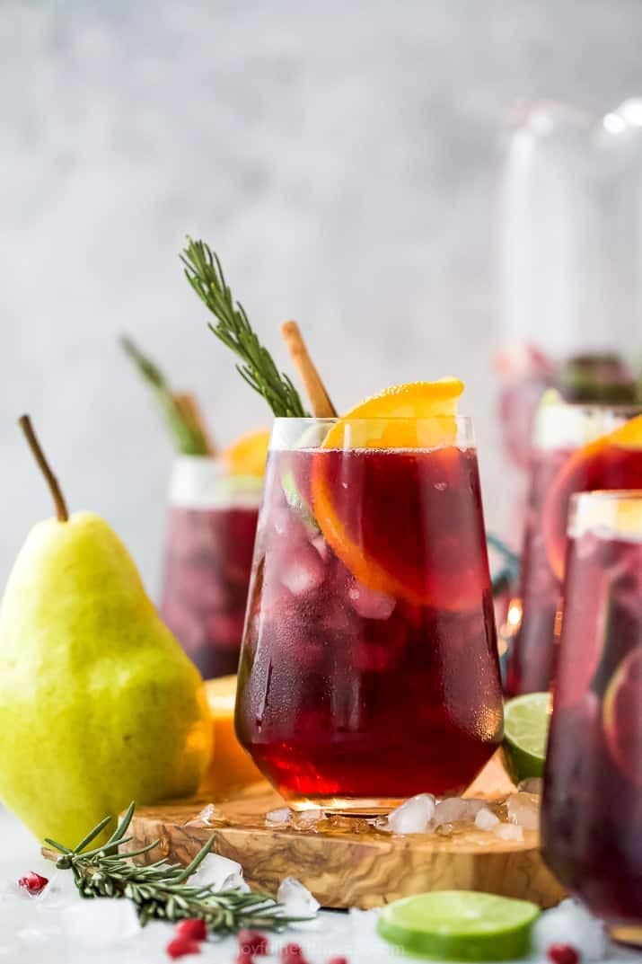 christmas-sangria Sangria cocktail served on tall glasses garnished with sliced lemon and rosemary leaves.