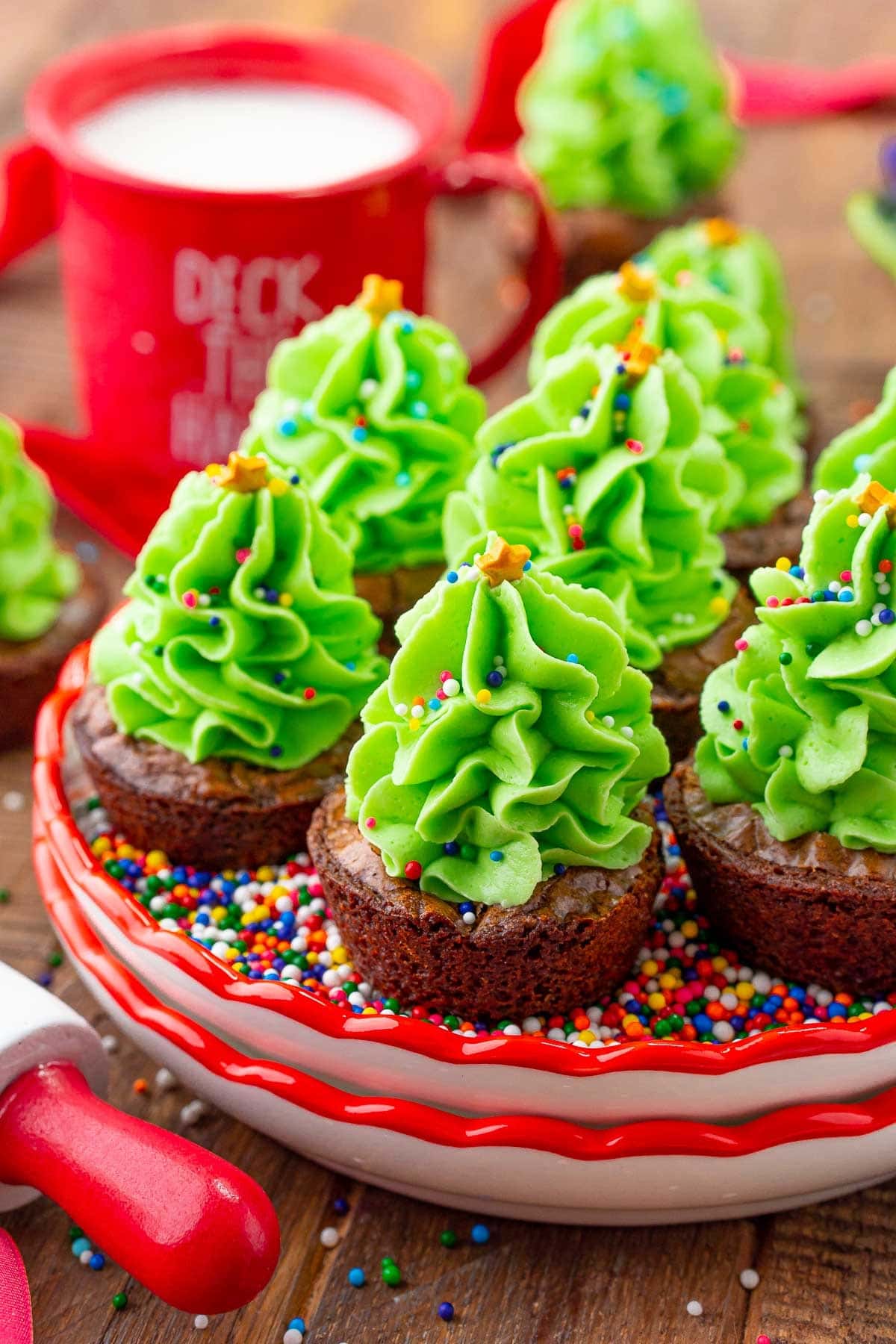 christmas-tree-brownie-bites Mini brownie cupcakes placed on a bed of sprinkles with green icing piping on top.