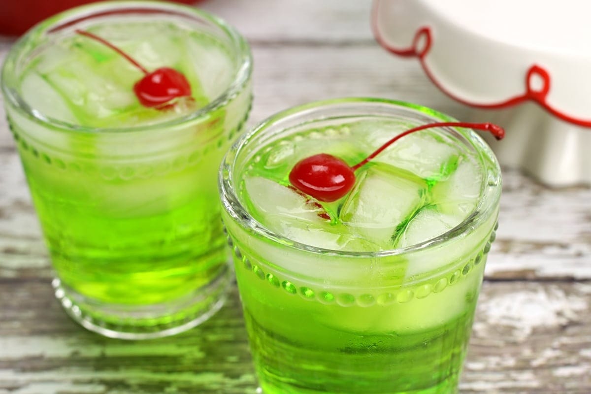 the-grinch-cocktail Two glasses of iced green cocktail garnished with cherry.