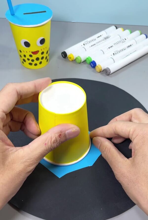 Placing Paper Cup Upside Down On Blue Paper - Design your own recycling craft with this easy-to-do craft.